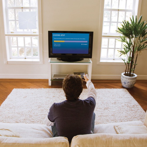 Person sitting on a couch in a living room running a channel scan on the television to maximize programming