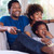 Man, woman and child sitting on a couch smiling while watching TV