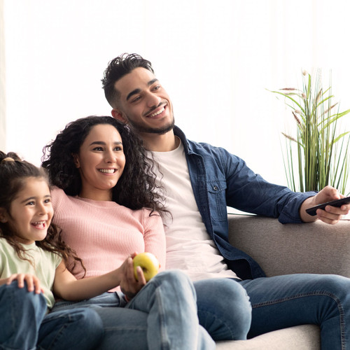 Man, woman and a child sitting on a couch smiling and watching TV together