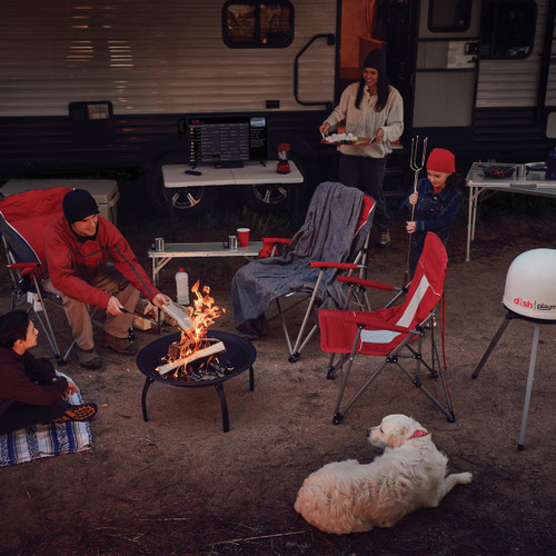 Family and dog sitting around a fire pit outside an RV with a TV on the table and a refurbished DISH Playmaker Portable Automatic Satellite Antenna on a tripod